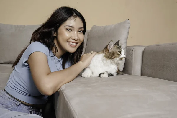 Pretty Asian woman hug a cat and sit on couch with happy emotion. Adorable domestic pet concept.