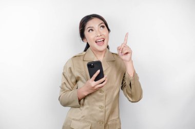 Gülümseyen devlet çalışanı kadın akıllı telefonunu tutuyor ve üstündeki kopyalama alanını işaret ediyor. Not: haki rengi üniforma giyiyor..