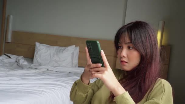 아시아의한 여성은 침실에 스마트폰을 진지하게 주의를 기울이고 — 비디오