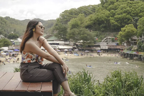 stock image Young Asian girl sitting on the edge of cliff above the sea hearing wind by herself. Holiday concept