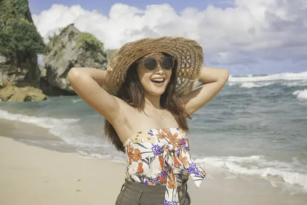 Plaj şapkası takan mutlu bir Asyalı kadın elleri açık kameraya poz veriyor. Gunungkidul, Endonezya sahilinde özgürlüğünü ve tasasız tatilini ifade ediyor.