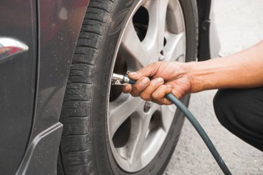 Klaten, Endonezya - 17 Ağustos 2023: Adam sürücü el arabası şişiren lastikler, hava basıncını kontrol etmek ve benzin istasyonundaki araba tekerleğinin havasını doldurmak için lastik valf kapağını kaldırmak.