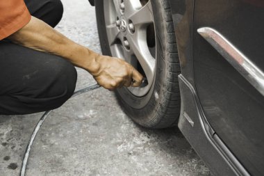 Klaten, Endonezya - 17 Ağustos 2023: Adam sürücü el arabası şişiren lastikler, hava basıncını kontrol etmek ve benzin istasyonundaki araba tekerleğinin havasını doldurmak için lastik valf kapağını kaldırmak.