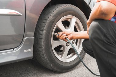 Klaten, Endonezya - 17 Ağustos 2023: Adam sürücü el arabası şişiren lastikler, hava basıncını kontrol etmek ve benzin istasyonundaki araba tekerleğinin havasını doldurmak için lastik valf kapağını kaldırmak.