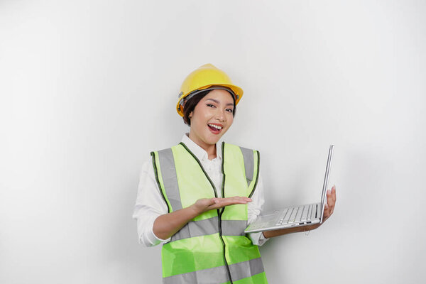 A smiling Asian woman labor wearing safety helmet and vest while holding her laptop, isolated by white background. Labor's day concept.
