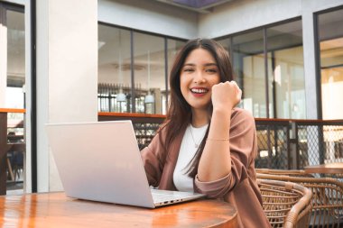 Uzaktan kumandayla çalışan gülümseyen Asyalı kadın bilgisayarını kullanıyor. Çalışanlar online video görüşmesi için hazırlanıyor.