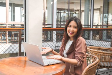 Uzaktan kumandayla çalışan gülümseyen Asyalı kadın bilgisayarını kullanıyor. Çalışanlar online video görüşmesi için hazırlanıyor.