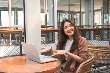 Uzaktan kumandayla çalışan gülümseyen Asyalı kadın bilgisayarını kullanıyor. Çalışanlar online video görüşmesi için hazırlanıyor.