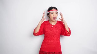 Kırmızı kebaya ve saç bandı takan şok olmuş Asyalı bir kadın ağzı açık, beyaz arka planla izole edilmiş. Endonezya 'nın bağımsızlık günü konsepti