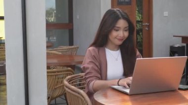 Uzaktan kumandayla çalışan gülümseyen Asyalı kadın bilgisayarını kullanıyor. Çalışanlar online video görüşmesi için hazırlanıyor.