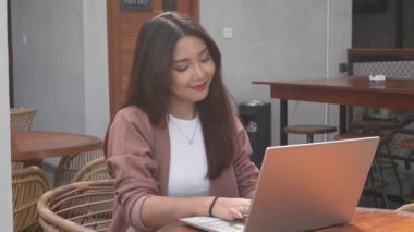 Uzaktan kumandayla çalışan gülümseyen Asyalı kadın bilgisayarını kullanıyor. Çalışanlar online video görüşmesi için hazırlanıyor.