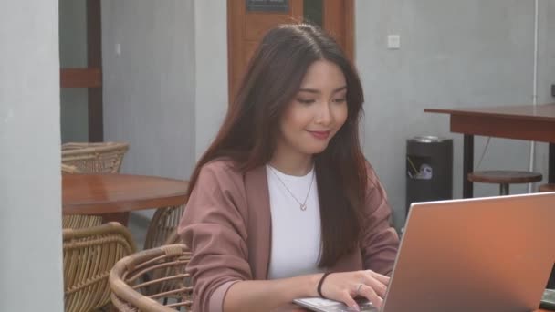 彼女のラップトップを使用してカフェからリモートで働く若いアジアの女性微笑み 従業員はオンラインビデオコールのインタビューの準備をしています — ストック動画