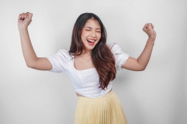 Sıradan kıyafetler giyen mutlu bir Asyalı kadın elleri açık kameraya poz veriyor. Özgürlüğünü ve tasasızlığını ifade ediyor.