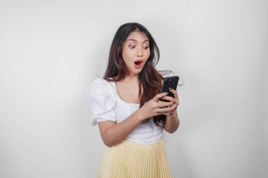 Beyaz arka planla izole edilmiş akıllı telefonunu tutarken ağzı açık, şok olmuş Asyalı bir kadın..