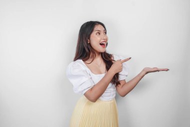 Neşeli bir Asyalı kadın beyaz arka planla izole edilmiş fotokopi alanını işaret ediyor..