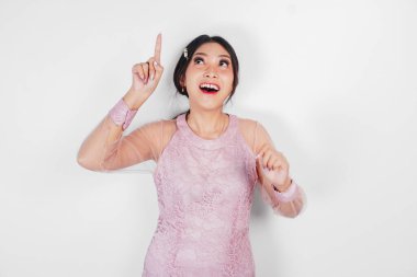 Pembe elbiseli gülümseyen Asyalı bir kadın, üst tarafındaki fotokopi alanını işaret ediyor, beyaz arka planla izole edilmiş..