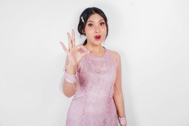 Pembe elbiseli çekici genç Asyalı kadın beyaz arka planla izole edilmiş parmaklarıyla işaret veriyor.