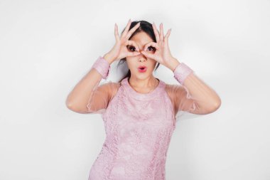 Pembe elbiseli çekici genç Asyalı kadın beyaz arka planla izole edilmiş parmaklarıyla işaret veriyor.