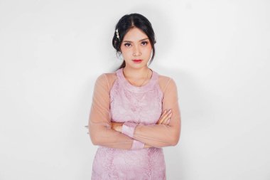Pembe elbiseli Asyalı genç bir kadın ellerini çaprazlarken ciddi bir ifade takınıyor.