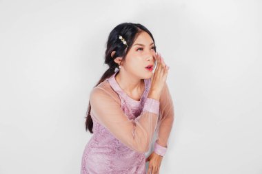 Genç ve güzel bir Asyalı kadın bağırıyor ve bağırıyor. Eli ağzında, beyaz arka planda izole bir şekilde..