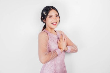 Pembe elbiseli arkadaş canlısı Asyalı kadın elleriyle geleneksel selamlar veriyor.