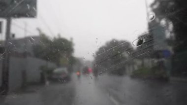 Şiddetli yağmurlu bir günün yoldaki görüntüsü, silecekler penceredeki yağmur damlacıklarını temizliyor ve bir arabanın içinden trafik manzarası var.