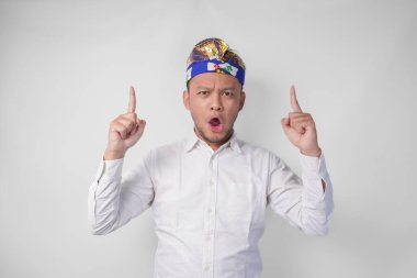 Geleneksel başlık takan Balili adam Udeng adındaki şaşırmış ve izole edilmiş beyaz arka planda fotokopi alanını yukarı doğru işaret ediyor.