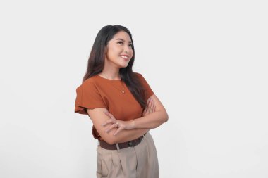 Kahverengi tişörtlü çekici genç Asyalı kadın kollarını çapraz yapıp izole edilmiş beyaz arka plan üzerinden yukarı bakıyor..