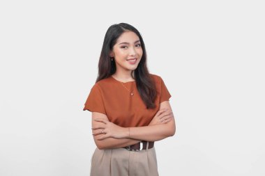 Kahverengi tişörtlü gülümseyen Asyalı kadın özgüven ifadesiyle beyaz arka planda izole edilmiş kameraya bakıyor..