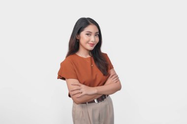 Kahverengi tişörtlü gülümseyen Asyalı kadın özgüven ifadesiyle beyaz arka planda izole edilmiş kameraya bakıyor..