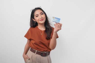 Kahverengi gömlek giyen kendine güvenen genç Asyalı kadın beyaz arka planda Endonezya kimlik kartını kameraya gösteriyor..