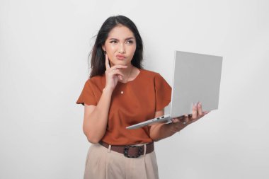 Kahverengi tişört giyen düşünceli genç bir kadın elinde dizüstü bilgisayarla beyaz arka planda izole bir şekilde yan tarafa bakıyor..