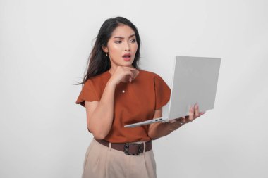 Kahverengi tişört giyen düşünceli genç bir kadın elinde dizüstü bilgisayarla beyaz arka planda izole bir şekilde yan tarafa bakıyor..