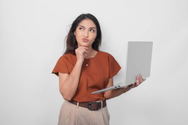 Kahverengi tişört giyen düşünceli genç bir kadın elinde dizüstü bilgisayarla beyaz arka planda izole bir şekilde yan tarafa bakıyor..