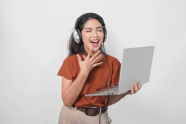 Surprised Young Woman Wearing Brown Shirt Headphone While Holding Laptop Stock Photo