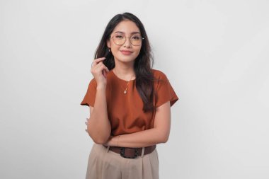 Kendine güvenen genç Asyalı kadın gülümseyip kameraya beyaz arka planda izole edilmiş zarif bir pozla bakıyor..