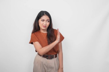 Kahverengi tişörtlü, üzgün genç Asyalı kadın dur işareti yapıyor. Avuç içi ile izole edilmiş beyaz arka plan..