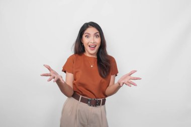 Kahverengi gömlek giyen heyecanlı ve şaşırmış genç bir Asyalı kadın beyaz arka planda tek başına dikiliyor..