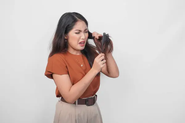 Attractive Asian Woman Brown Shirt Feeling Upset While Using Haircomb stockbilde