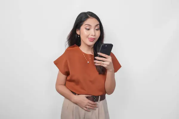白い背景の上に隔離されたスマートフォンを保持しながら脇に見える茶色のシャツを着ている空腹の若い女性 ロイヤリティフリーのストック画像