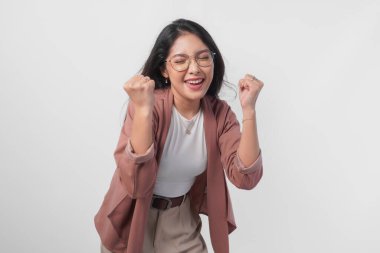 Başarılı bir galibiyet jesti yapan neşeli genç Asyalı kadın izole edilmiş beyaz arka planda yumruğunu sıktı..