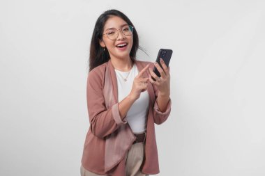 Gözlüklü gülümseyen Asyalı kadın, beyaz arka planla izole edilmiş internete mesaj atmak veya göz atmak için telefon kullanıyor..