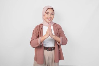 Peçe takan zarif Asyalı Müslüman kadın kameraya gülümsüyor ve beyaz arka planda izole edilmiş geleneksel selamlaşmaları işaret ediyor..