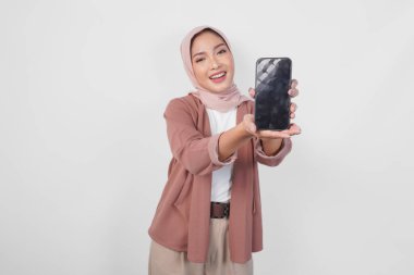 Genç Asyalı tesettürlü Müslüman kadın tesettüre gülümserken, beyaz arkaplan tarafından izole edilmiş akıllı telefon ekranında kopya alanı gösteriyor..