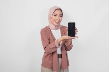 Genç Asyalı tesettürlü Müslüman kadın tesettüre gülümserken, beyaz arkaplan tarafından izole edilmiş akıllı telefon ekranında kopya alanı gösteriyor..