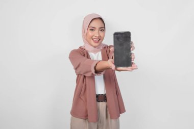 Genç Asyalı tesettürlü Müslüman kadın tesettüre gülümserken, beyaz arkaplan tarafından izole edilmiş akıllı telefon ekranında kopya alanı gösteriyor..