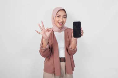 Tesettürlü genç Asyalı Müslüman kadın telefon ekranında fotokopi odasını gösteriyor ve hoş bir jest yapıyor, beyaz arkaplanla izole edilmiş..