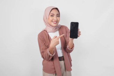 Mutlu Asyalı Müslüman kadın tesettürde gülümsüyor ve akıllı telefonunda beyaz arka planla izole edilmiş fotokopi alanı gösteriyor..