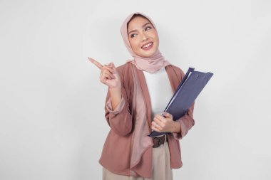 Tesettürlü neşeli, genç, Müslüman, Asyalı bir kadın, beyaz arkaplan ile izole edilmiş, yukarı doğru kopyalama alanını işaret ediyor..