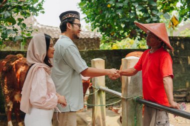 Genç Asyalı Müslüman çift sığırcıyla tokalaşıyor ve kurbanlık sığır almak için para veriyorlar. Kurban Bayramı kavramı.